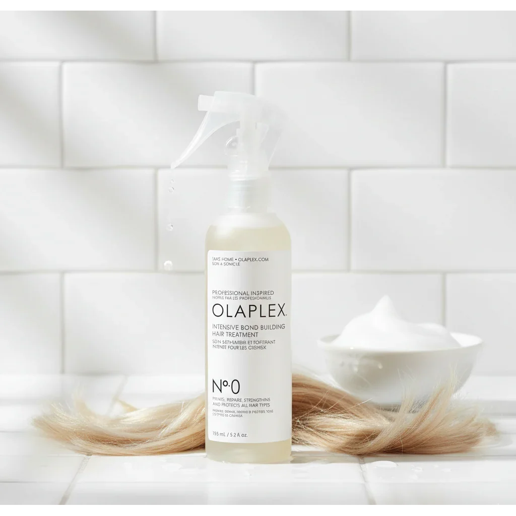 Olaplex No.0 hair treatment spray bottle with blonde hair, foam, and white tile background