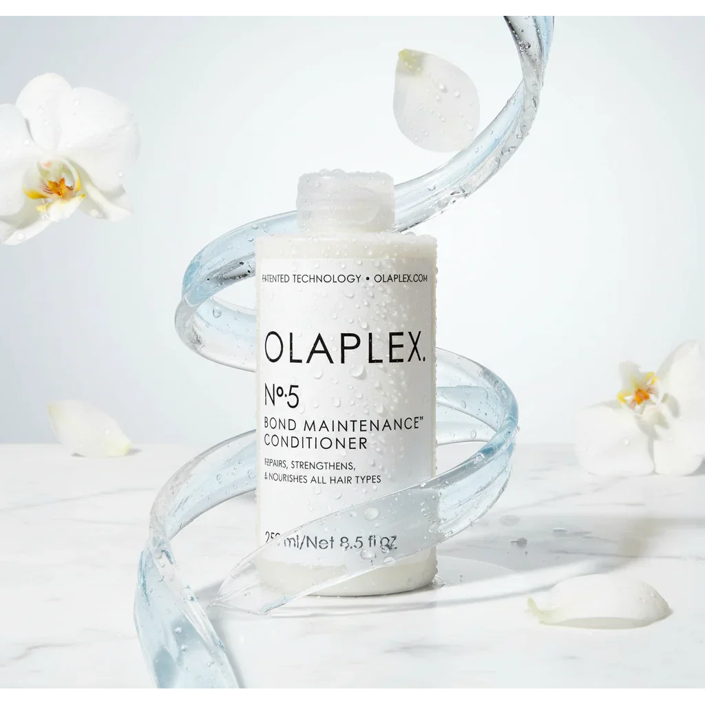 Olaplex No. 5 Bond Maintenance Conditioner with water droplets, white orchid flowers, and swirling blue liquid on a clean background.