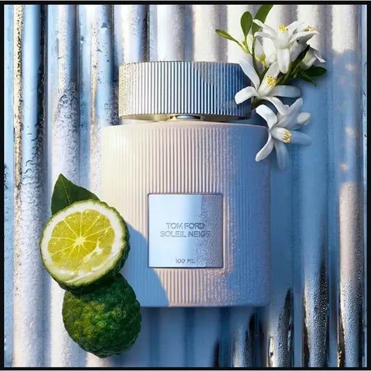 Tom Ford Soleil Neige perfume bottle with sliced lime and white flowers on a metallic background