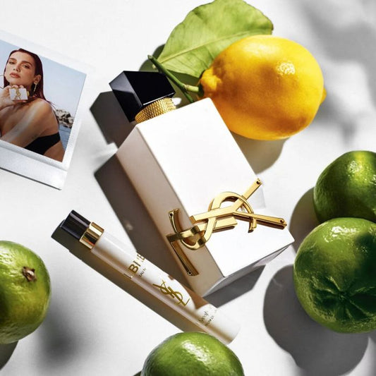 Elegant white perfume bottle with gold accents, citrus fruits, and a travel spray on a white background