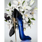 Elegant blue high heel perfume bottle with gold stiletto heel, white flowers in background
