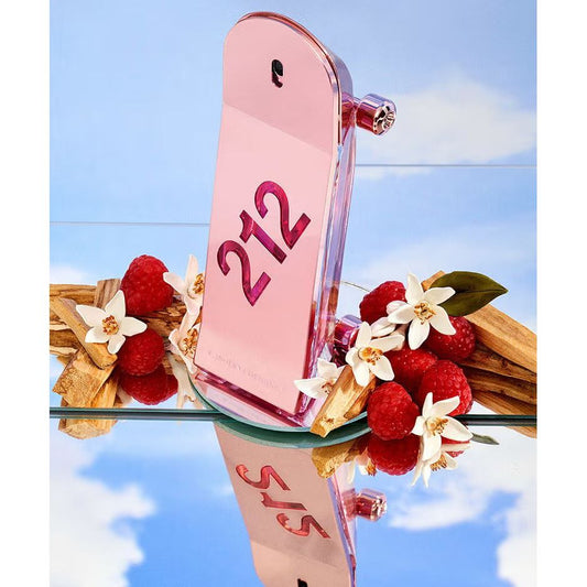 Pink perfume bottle with '212' on it, surrounded by raspberries, white flowers, and wood on a mirrored surface