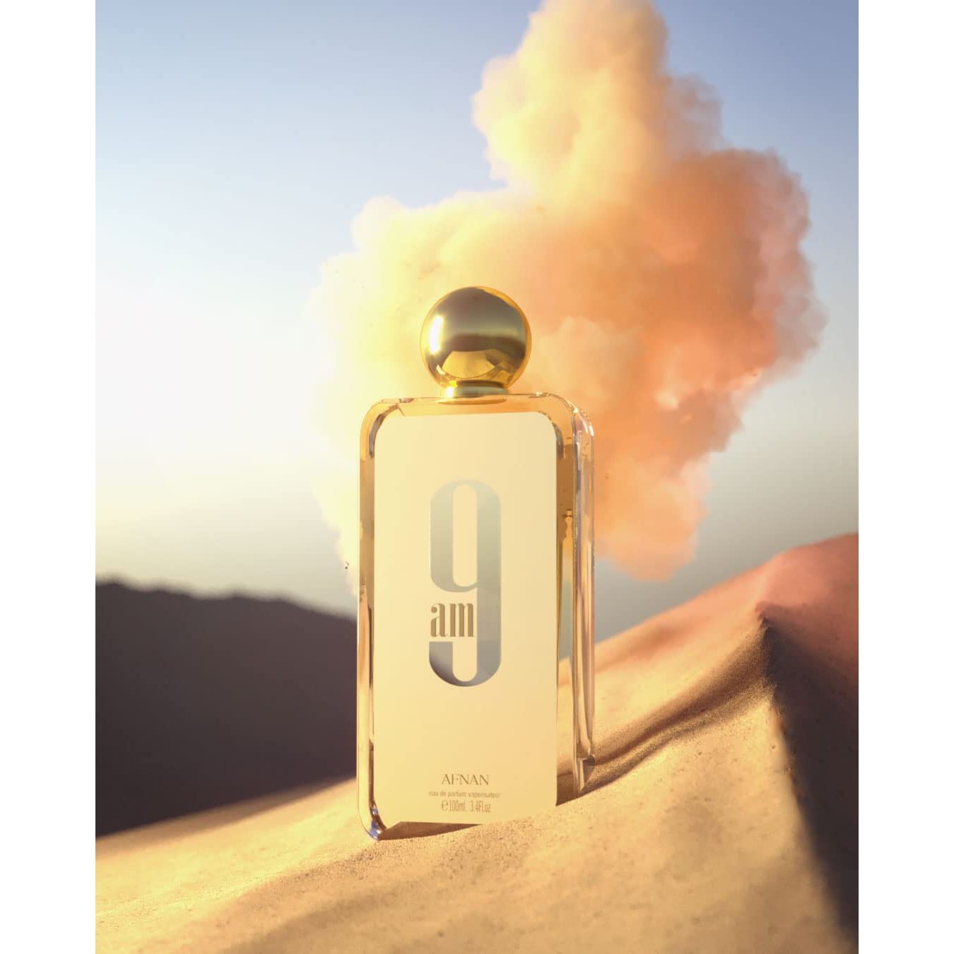 Afnan 9am perfume bottle on sand with sunrise sky and orange cloud, luxury fragrance