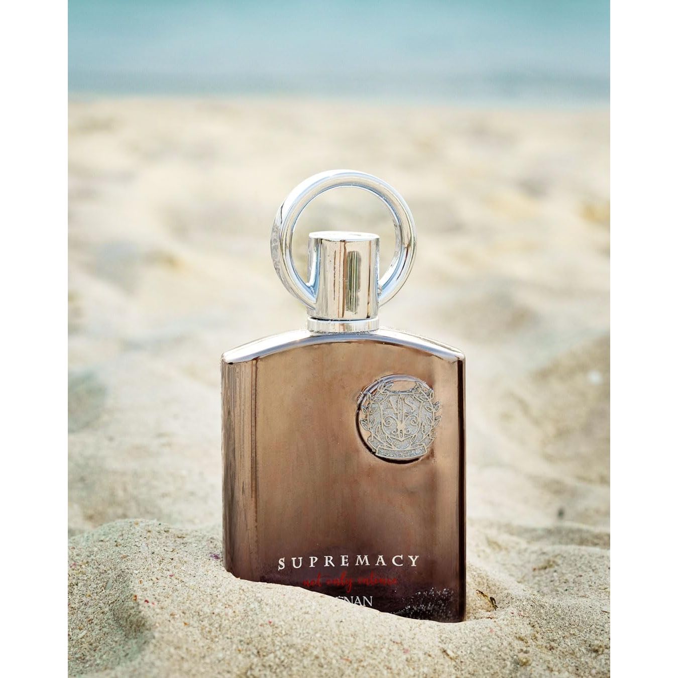 Luxury Supremacy perfume bottle on sandy beach, featuring elegant design and Arabic-inspired fragrance.