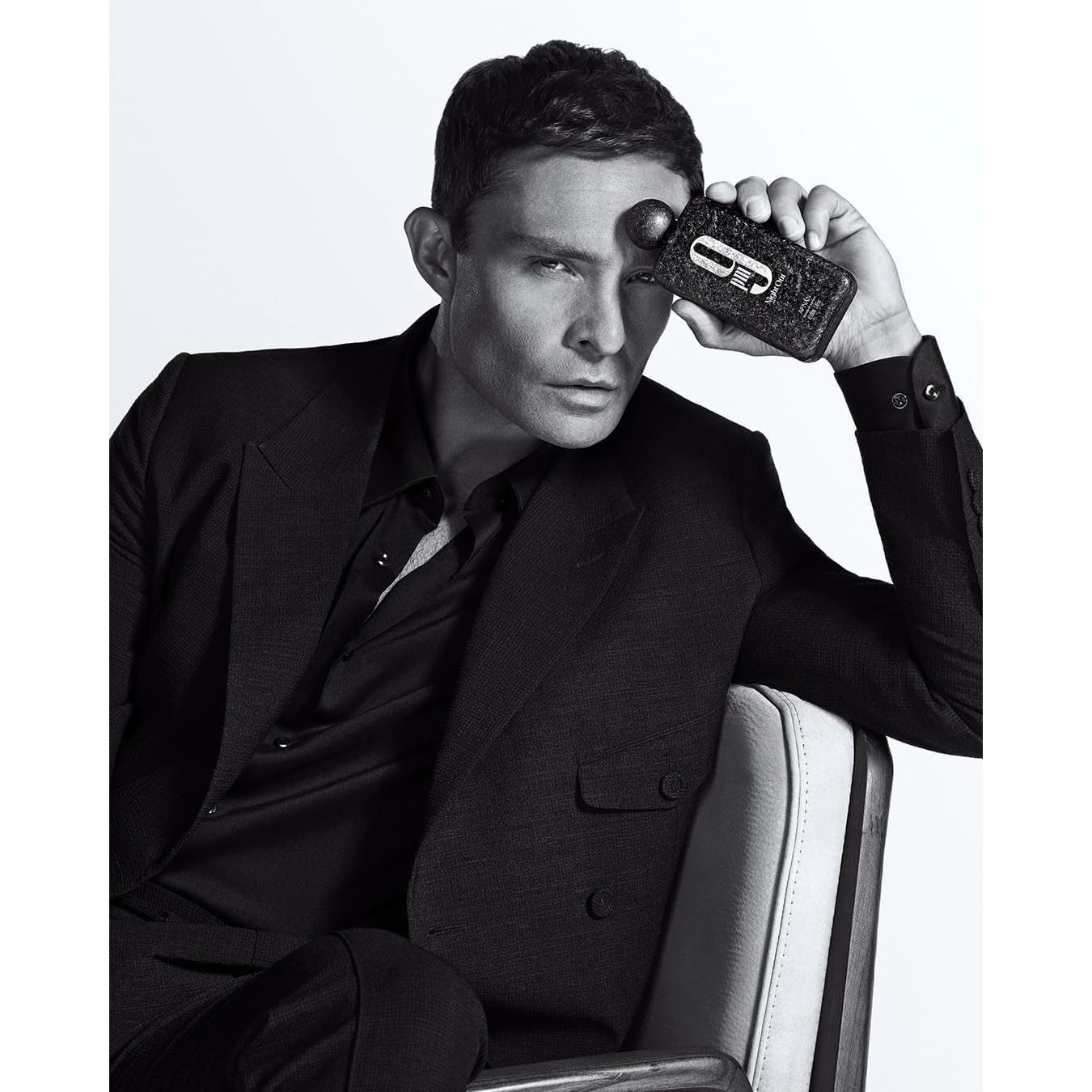 Man in black suit holding perfume bottle near his face in a modern portrait