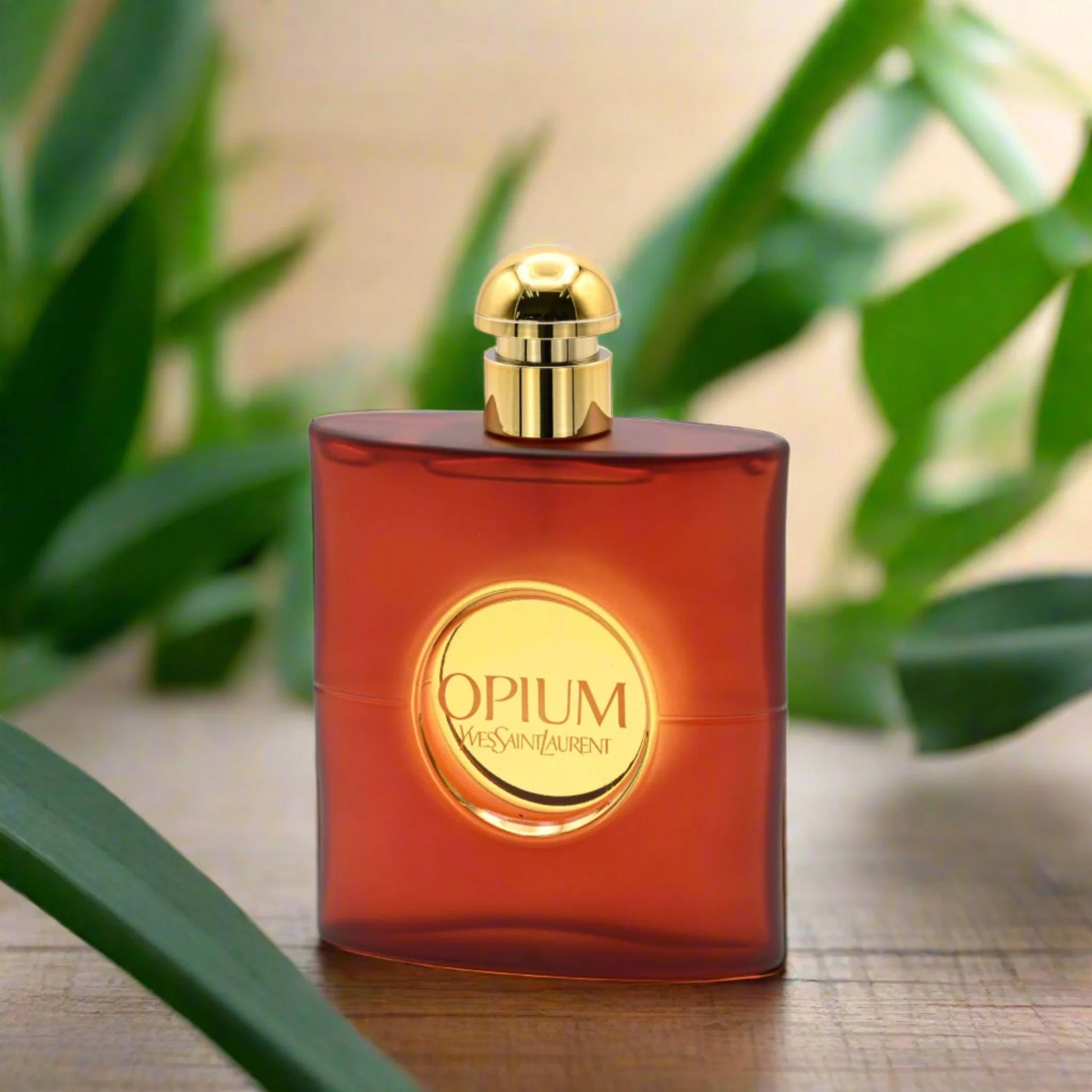 Yves Saint Laurent Opium perfume bottle with gold cap on wood surface, green leaves backdrop