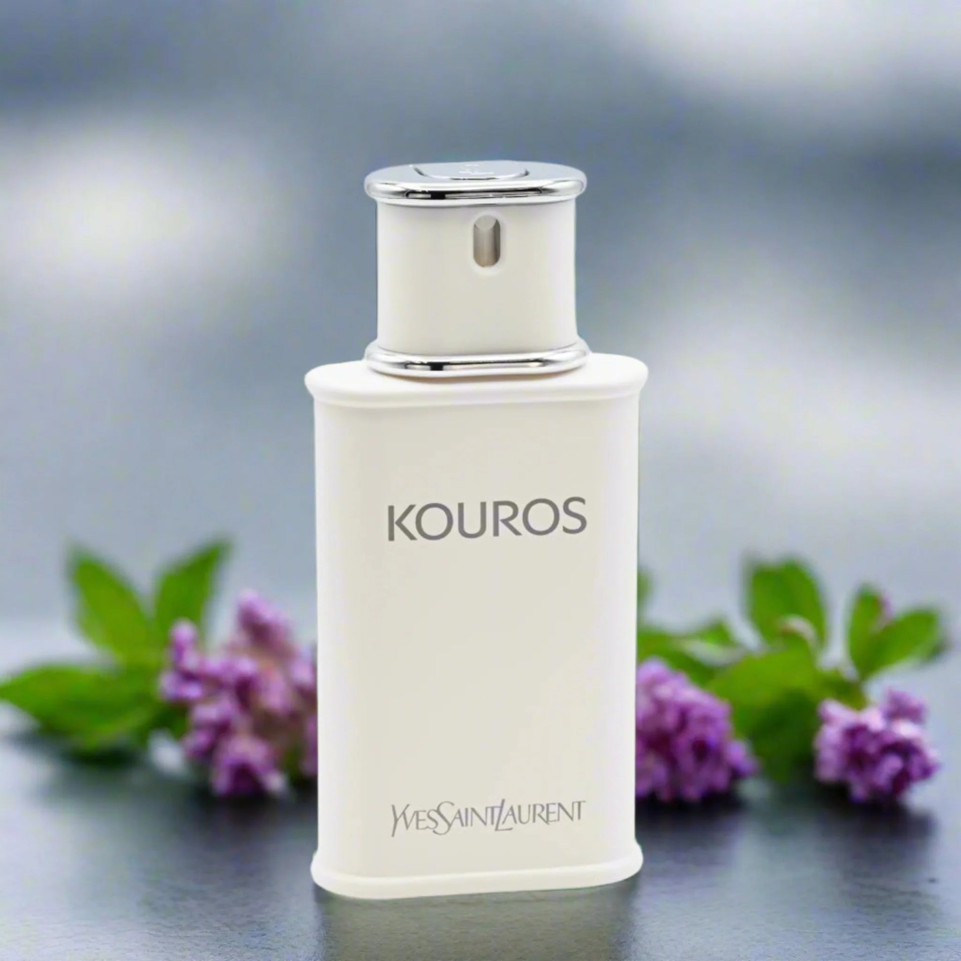 KOUROS white perfume bottle with silver accents beside purple flowers and green leaves